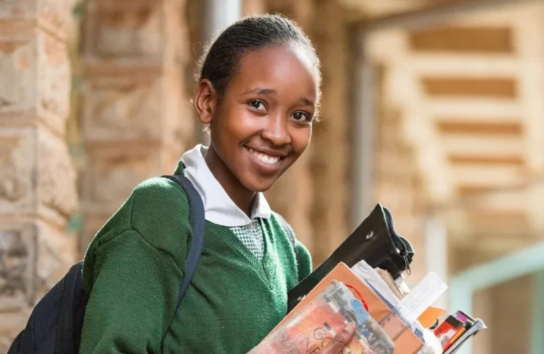 Kenyan woman student holding books, wearing a uniform happily and smiling at the camera