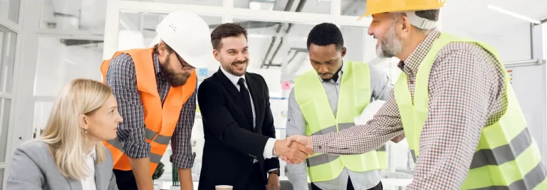 engineers in a team. two of them are shaking hands and smiling at each other