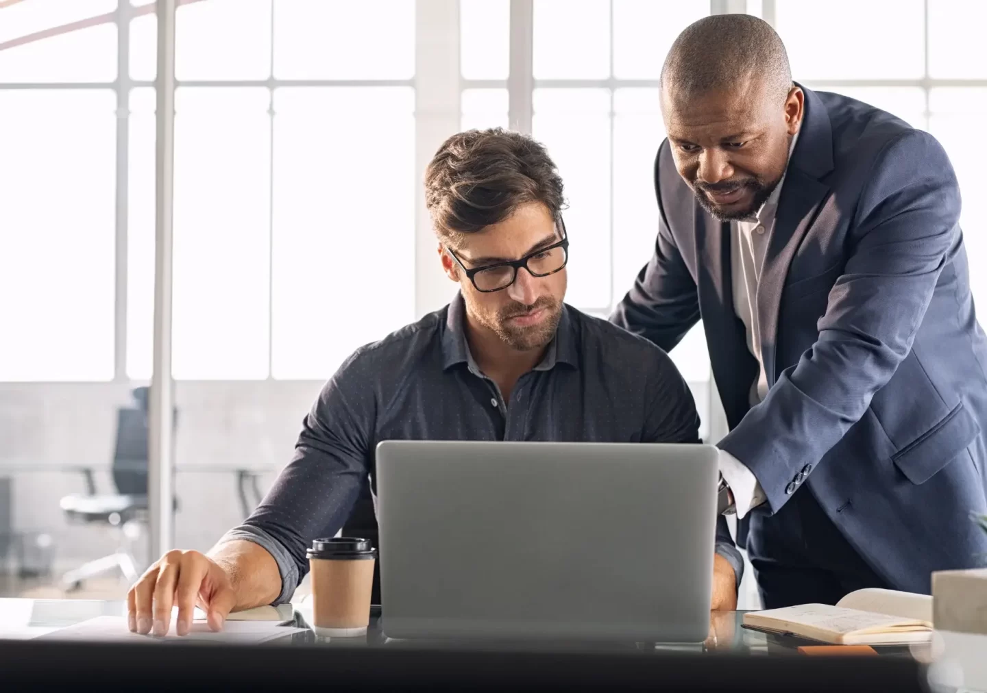 Two business professionals collaborating over a laptop in a modern office setting, representing EOR in UAE. The interaction highlights effective teamwork and mentorship, showcasing the supportive and dynamic work environment in the United Arab Emirates.