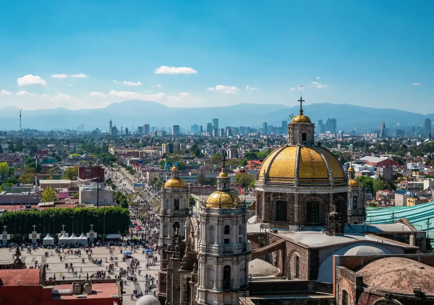 A panoramic view of Mexico City showcasing the iconic Basilica of Our Lady of Guadalupe with its golden domes, representing EOR in Mexico. The bustling cityscape with modern buildings and mountains in the background highlights the blend of historic and contemporary elements in Mexico.