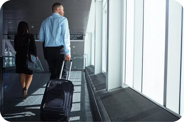 A professional walking through an airport with luggage, illustrating the global reach and responsibilities of an employer of record service.