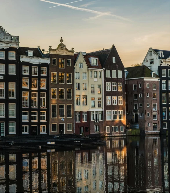 A scenic view of traditional canal houses reflecting on the water at sunset in Amsterdam, representing EOR in the Netherlands. The historic architecture and serene canal emphasize the country's unique cultural and business landscape.